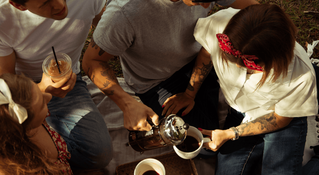 friends pouring a french press coffee on a picnic