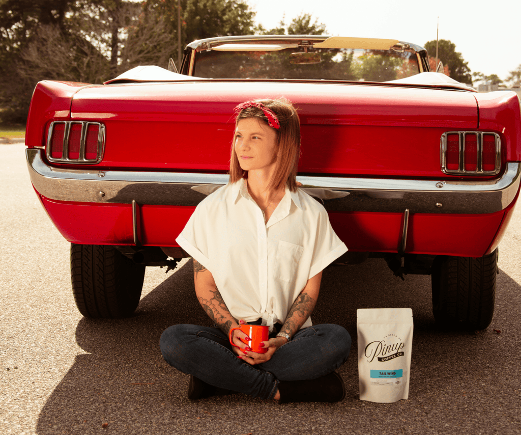Woman holding coffee mug in front of vintage car with coffee bean bag