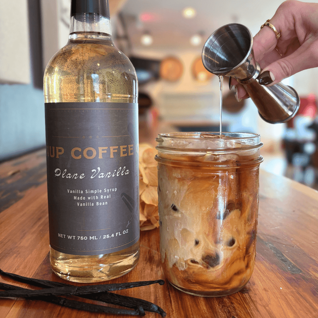 Bottle of vanilla simple syrup being poured into a jar of iced coffee.